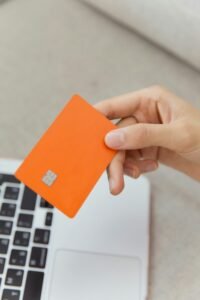 Close-up shot of an orange credit card held above a laptop, emphasizing digital payment.